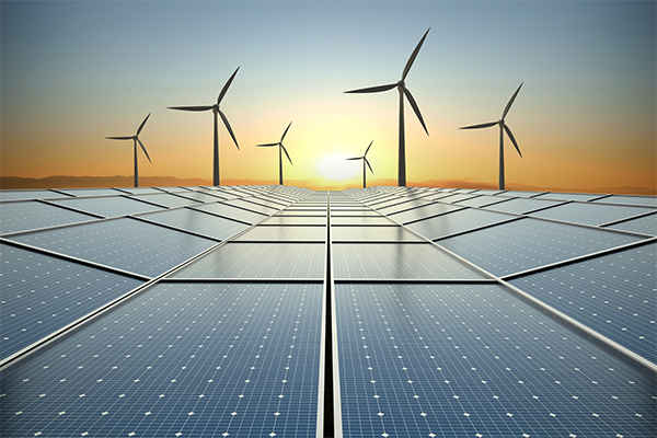 A field with multiple solar panels and wind turbines in the distance.